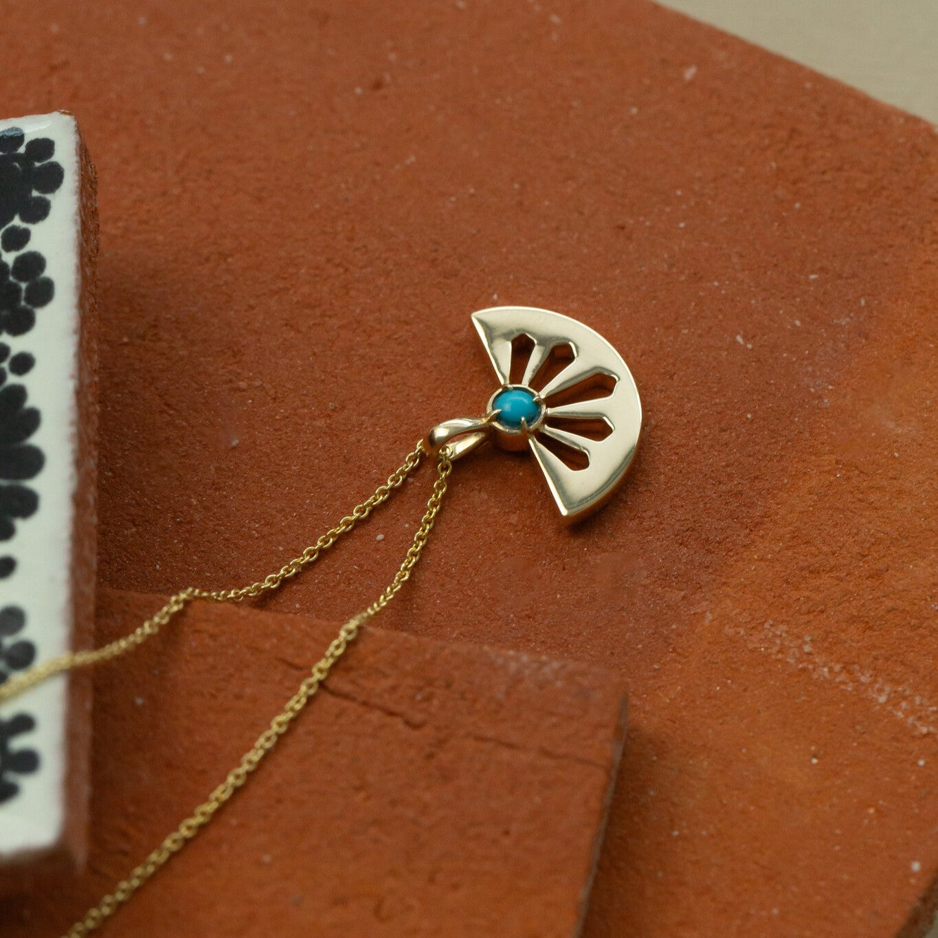 Gold necklace with a fan-shaped pendant featuring a blue gemstone on a brown surface.