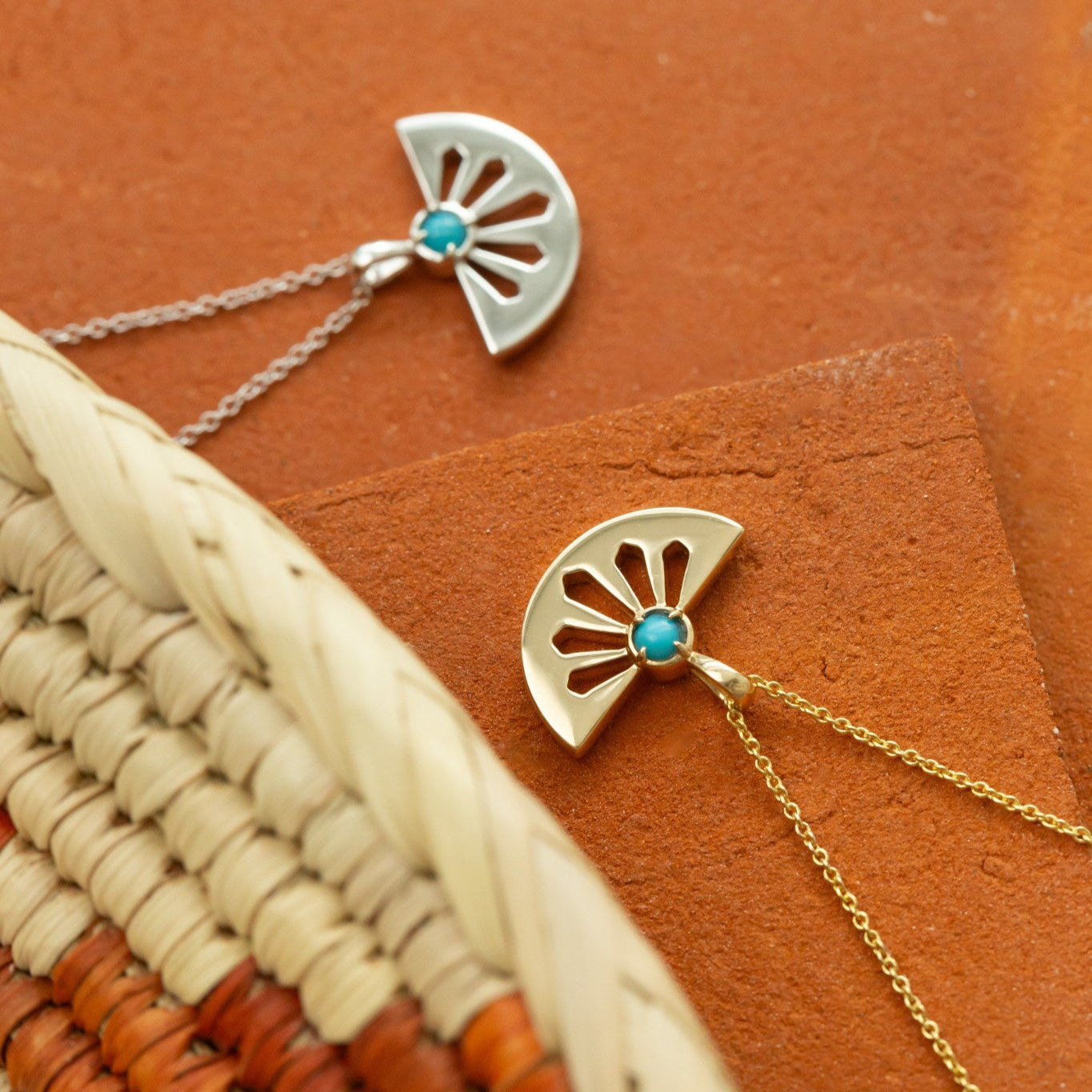 Two gold necklaces with turquoise stones on a textured brown surface.