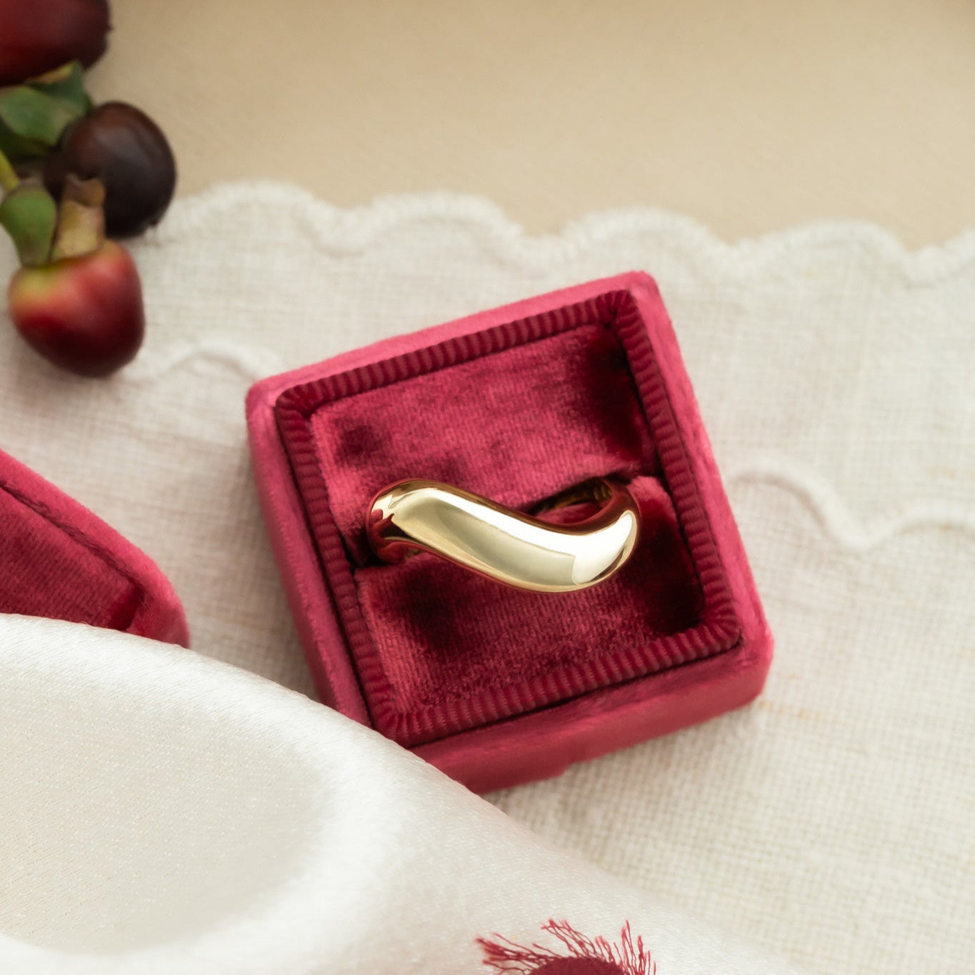 A 14k gold ring with a swooped rounded band, displayed in a red velvet box on a white surface.