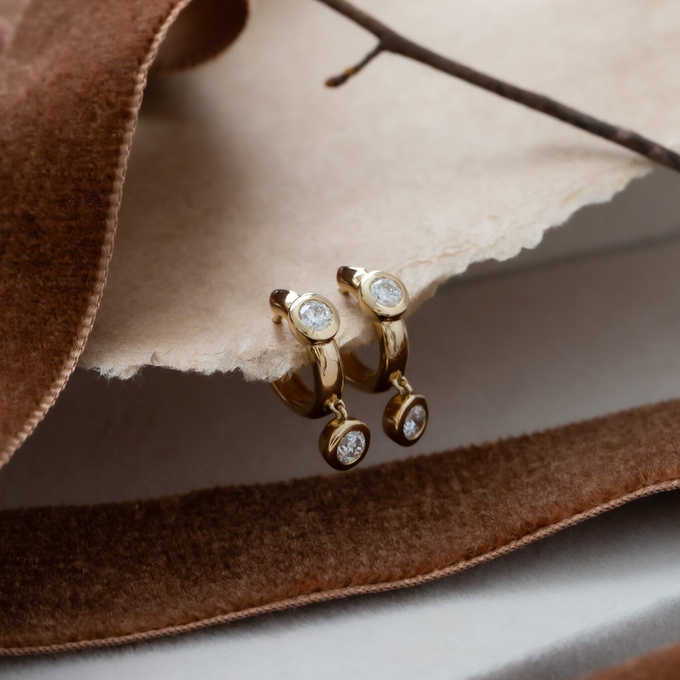 A pair of 14k yellow gold huggie earrings with round diamonds set on thick gold hoops, displayed on a brown velvet surface.