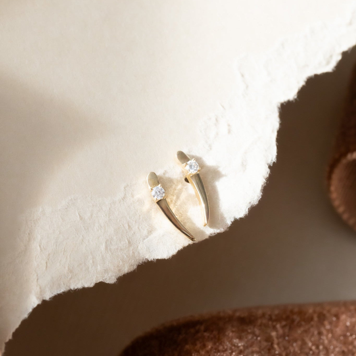 A close-up image of a pair of 14k yellow gold stud earrings with diamonds set on curved tapered gold bars, featuring friction backs and posts.