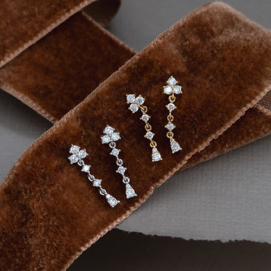 A pair of 14k gold dangle diamond earrings with a cluster design, displayed on a textured surface.