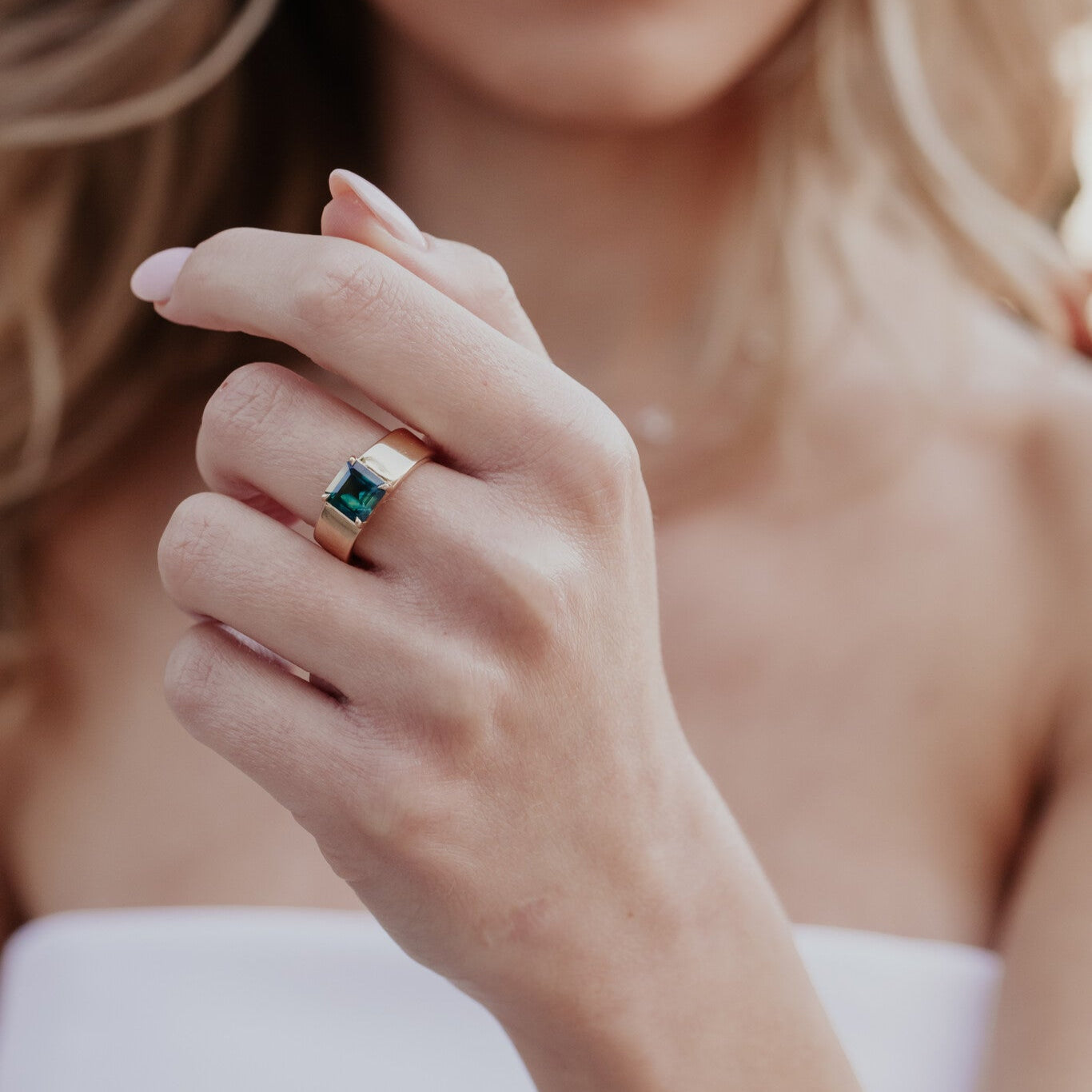 Close-up of a woman's hand wearing a ring with a green sapphire gemstone.