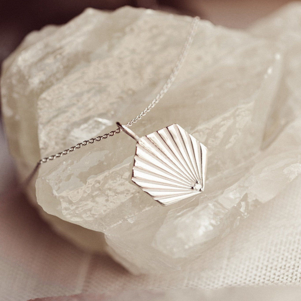 White gold shell charm necklace on a white stone surface