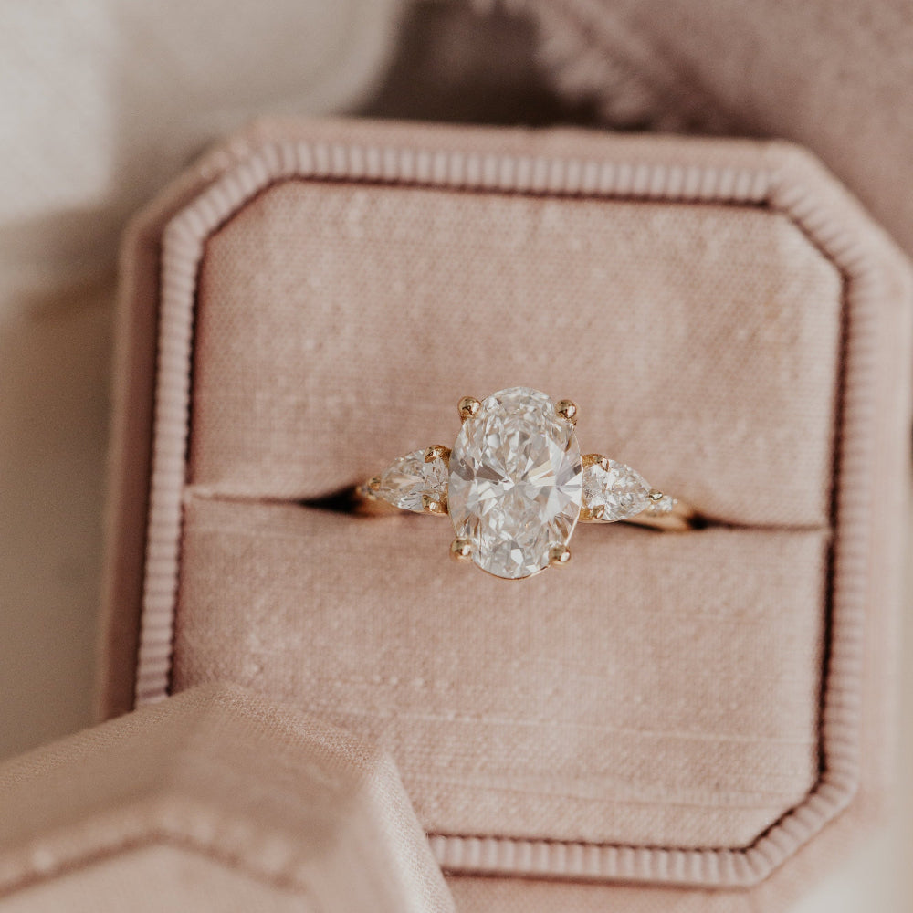The Toula oval diamond ring with pear and round diamond side stones in a rose gold band, displayed in a pink velvet ring box.