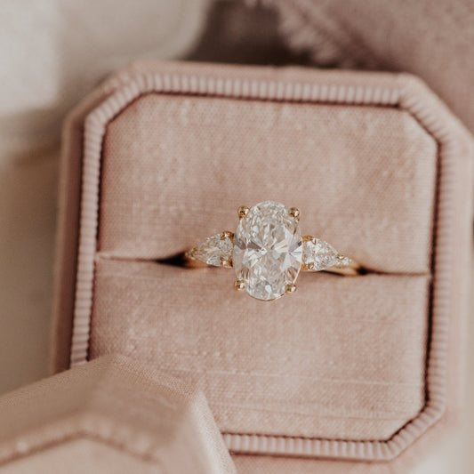 The Toula oval diamond ring with pear and round diamond side stones in a rose gold band, displayed in a pink velvet ring box.