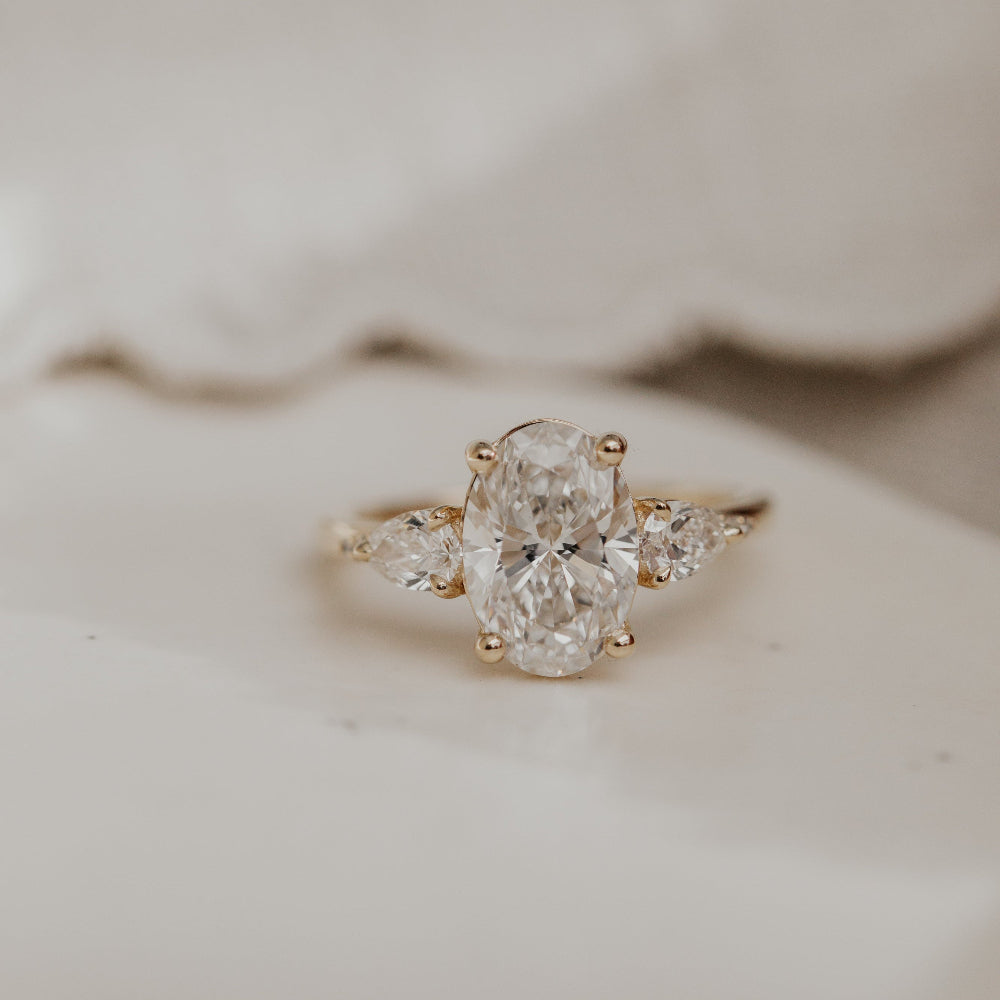 Close up of the Toula oval diamond engagement ring on a white surface.