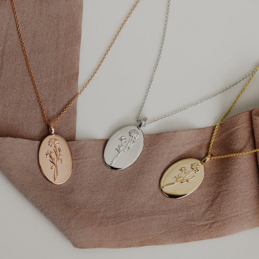 Three wildflower necklaces in rose gold, white gold, and yellow gold colors, displayed on a fabric surface.