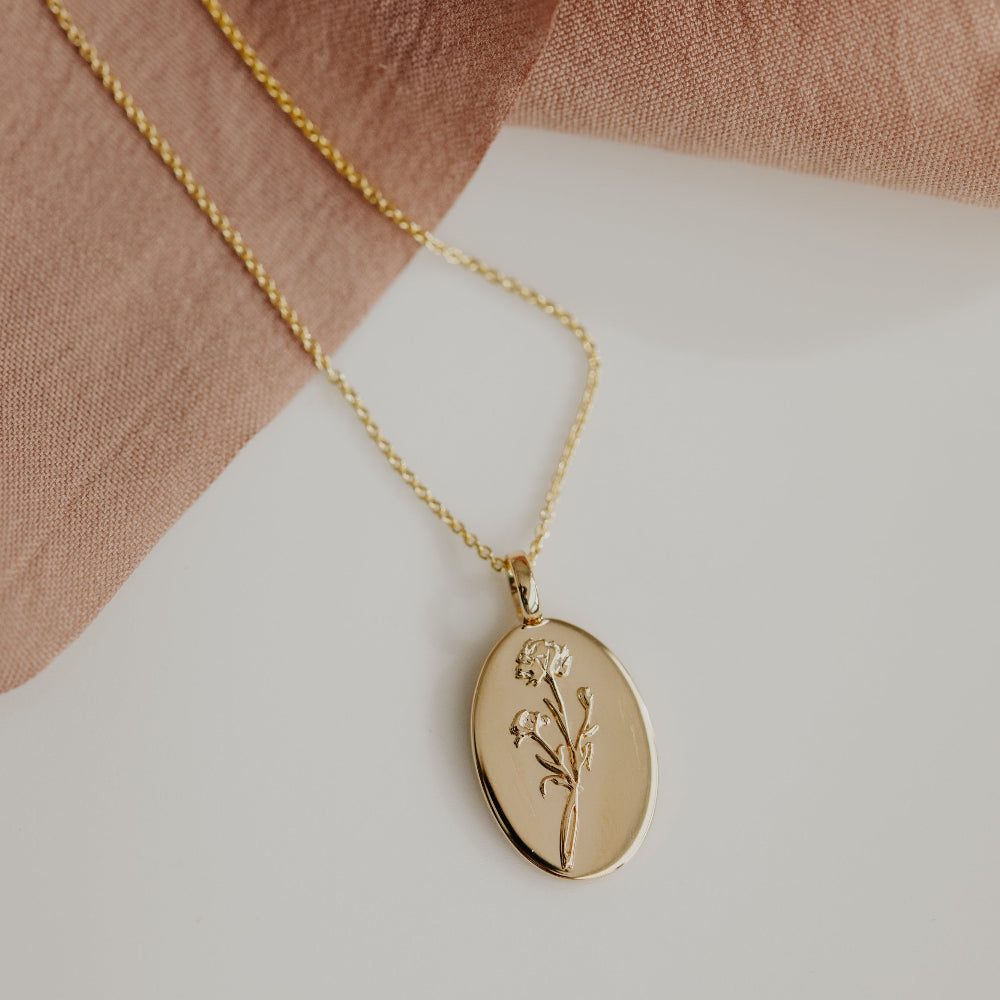 Gold necklace with an oval pendant featuring a floral design on a light background