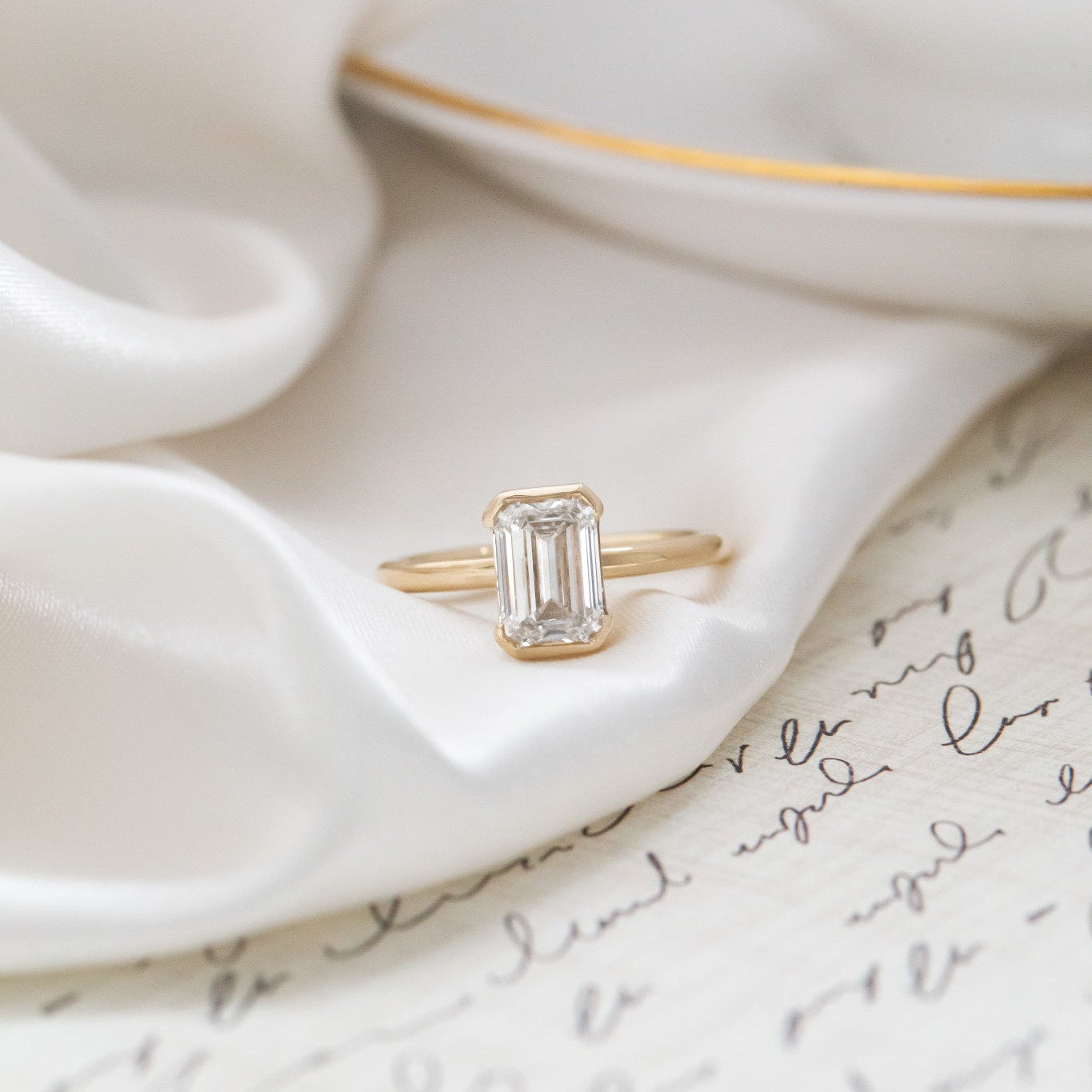 Zadie emerald cut diamond engagement ring on a white silk fabric.