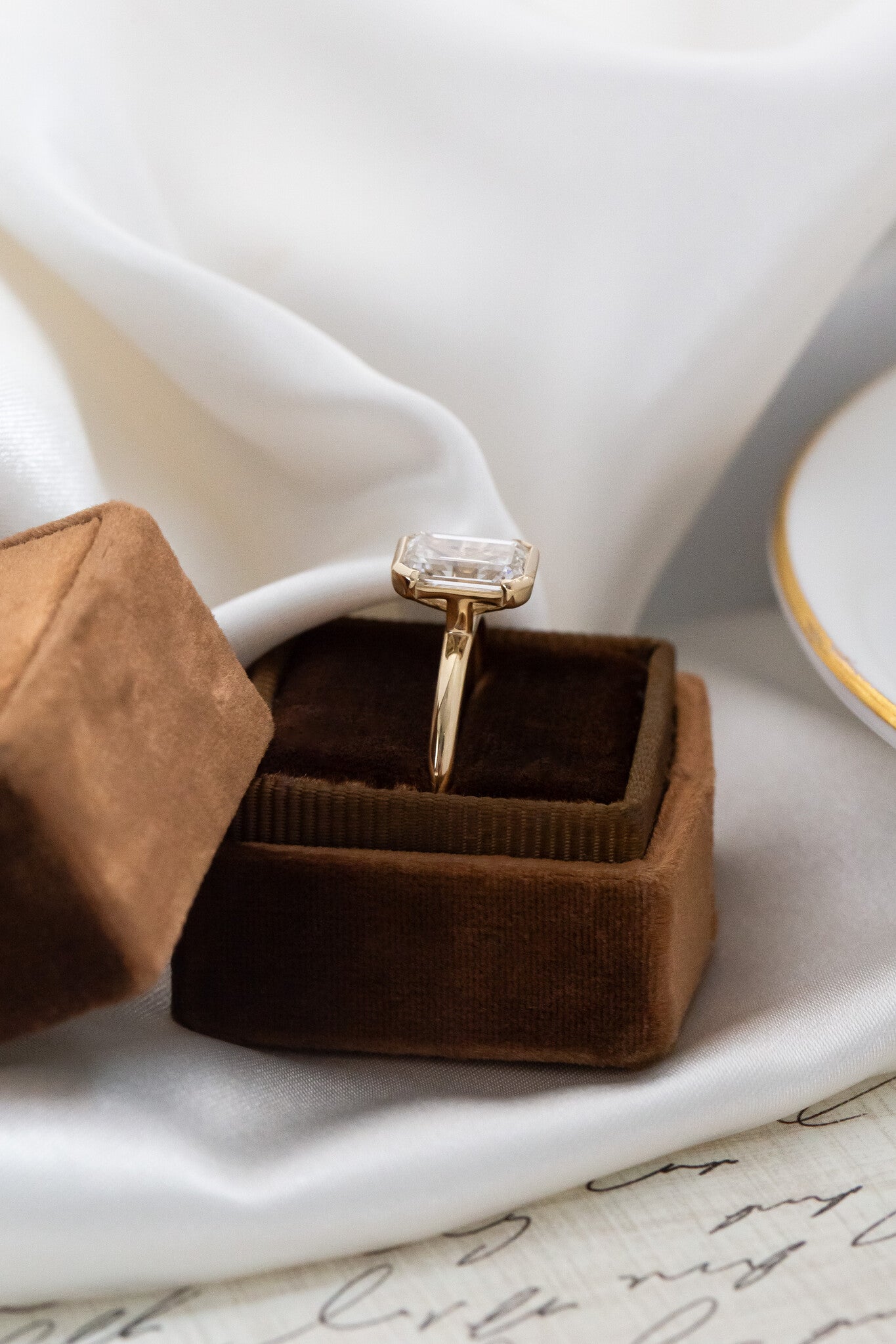 Side profile of the Zadie emerald cut diamond engagement. ring in a brown velvet ring box.