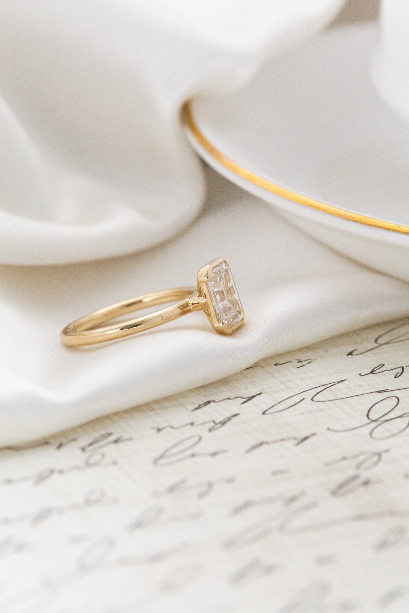 Side profile of the Zadie emerald cut diamond ring on a white silk fabric.