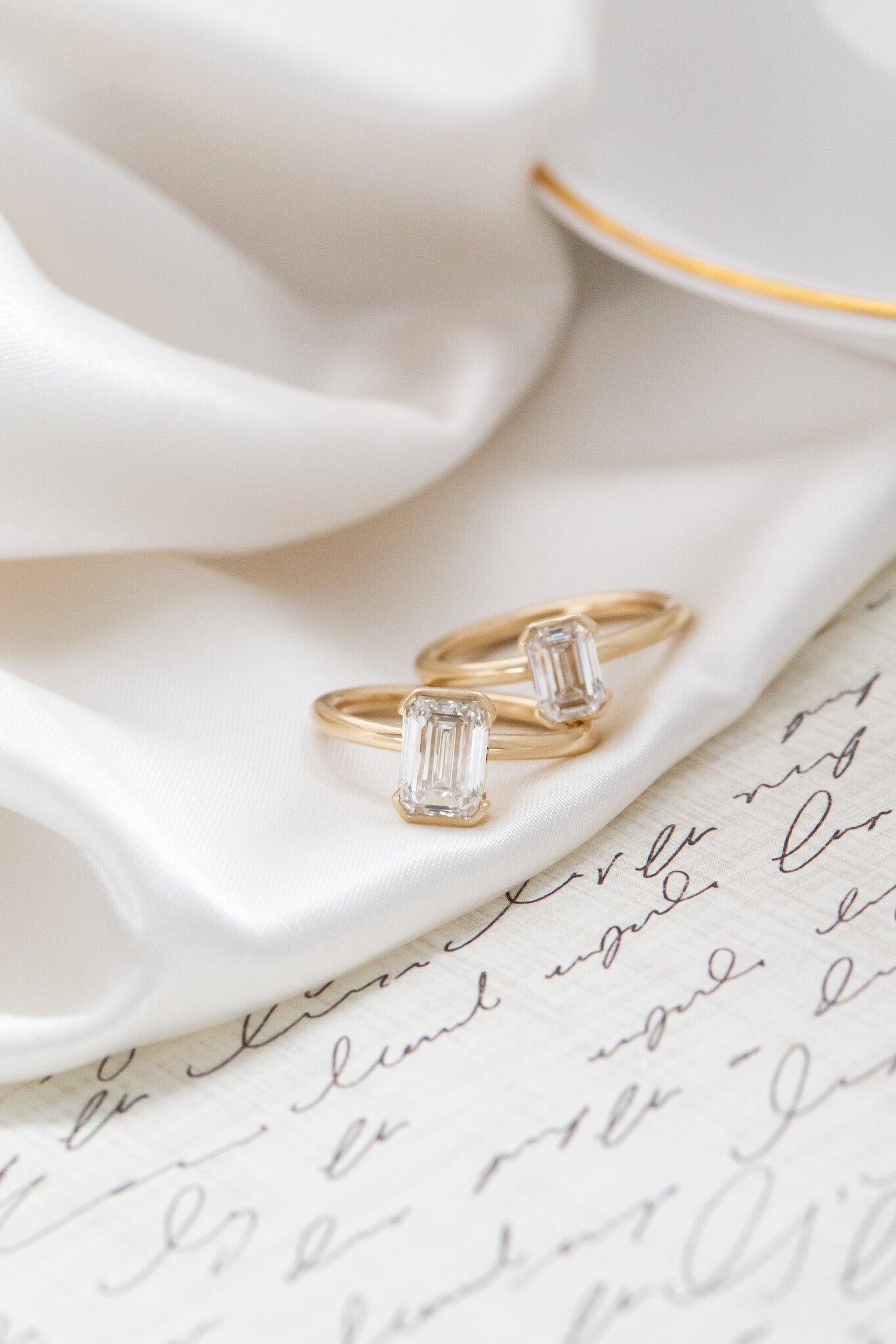 Two Zadie emerald cut diamond ring in different carat weights placed on a white silk fabric.