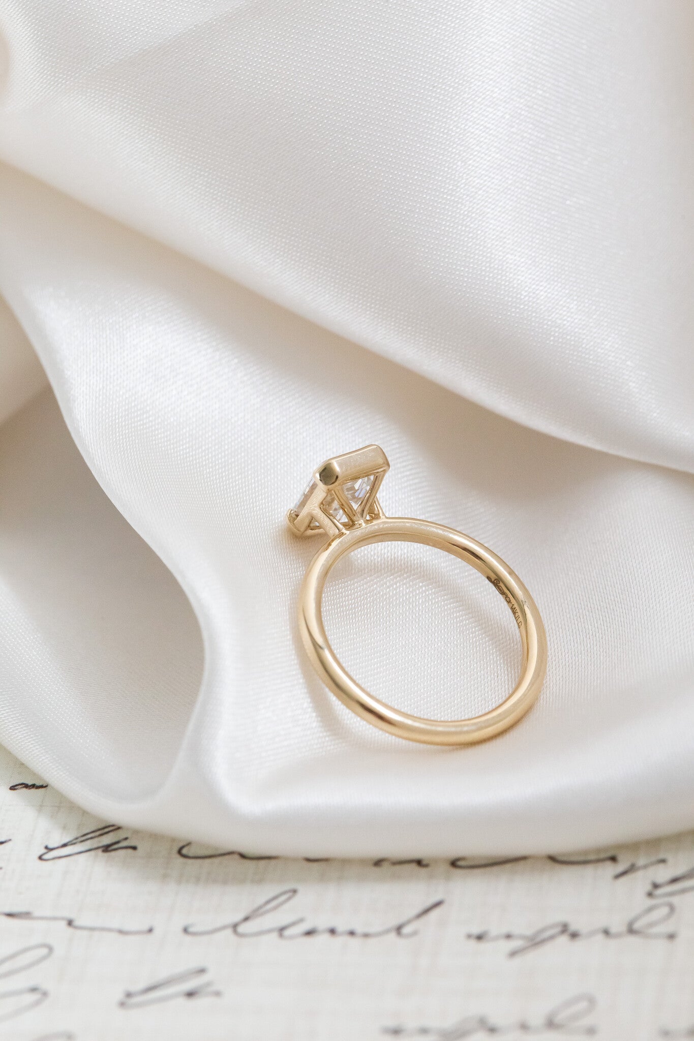 Gold band of the Zadie emerald cut diamond ring on a white silk fabric.
