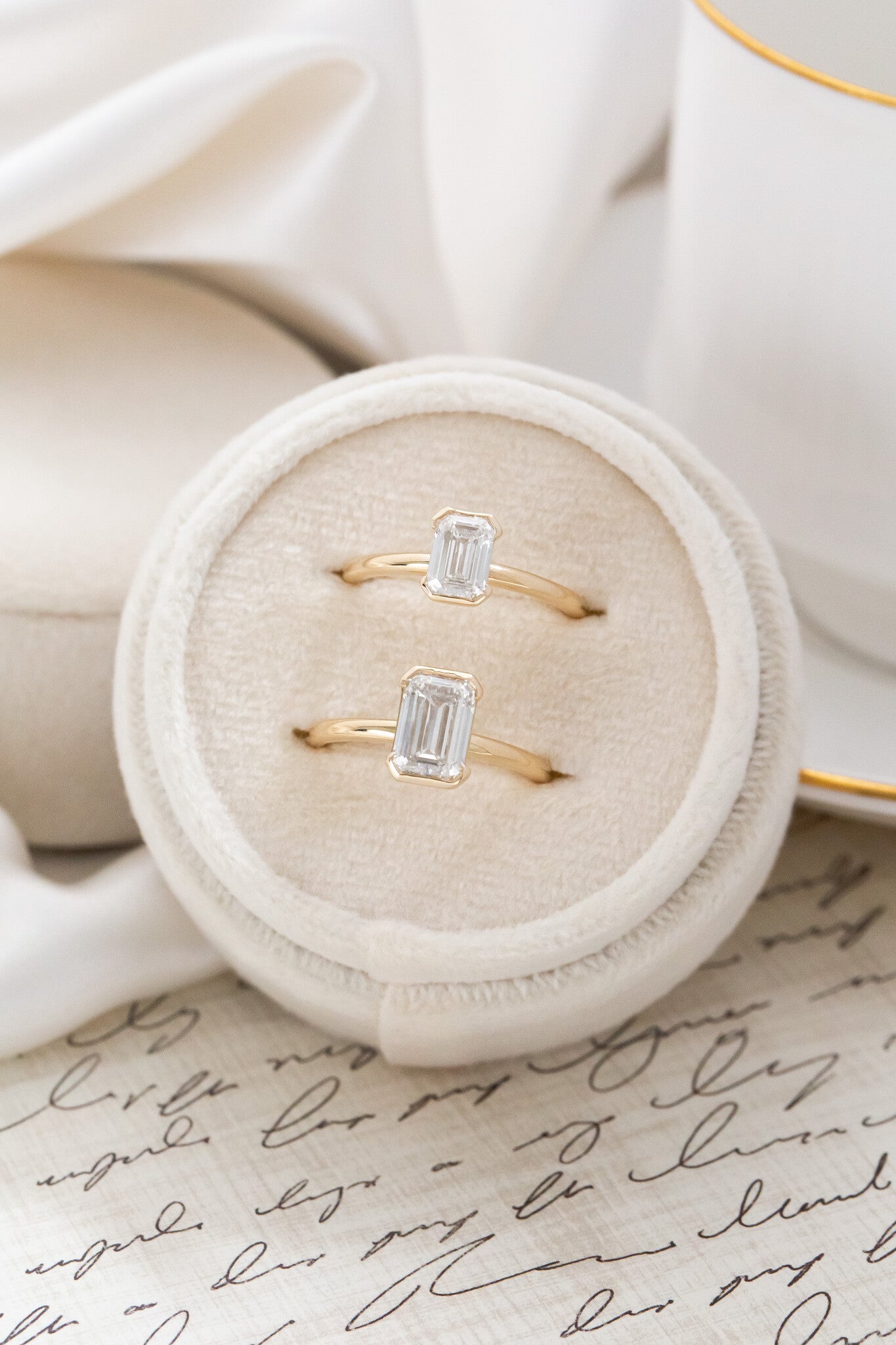 Two Zadie emerald cut diamond engagement ring in different carat weights placed in a white velvet ring box.