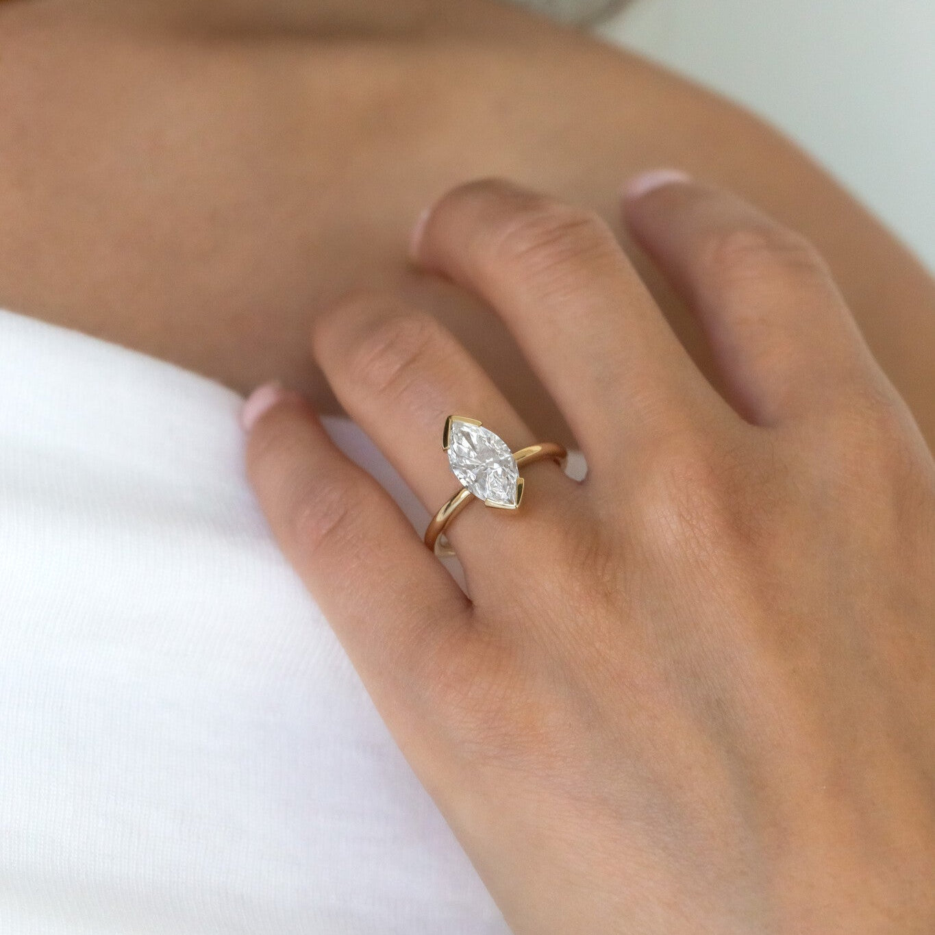 A Zadie marquise solitaire ring on a person's hand, with a white diamond set in a gold band, displayed in a natural lighting setting.