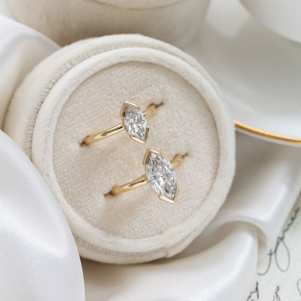 Two yellow gold Zadie marquise diamond solitaire engagement ring in different carat weights placed in a white jewelry box.