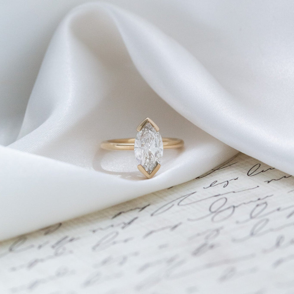 Gold Zadie engagement ring with a marquise diamond on a white fabric background.