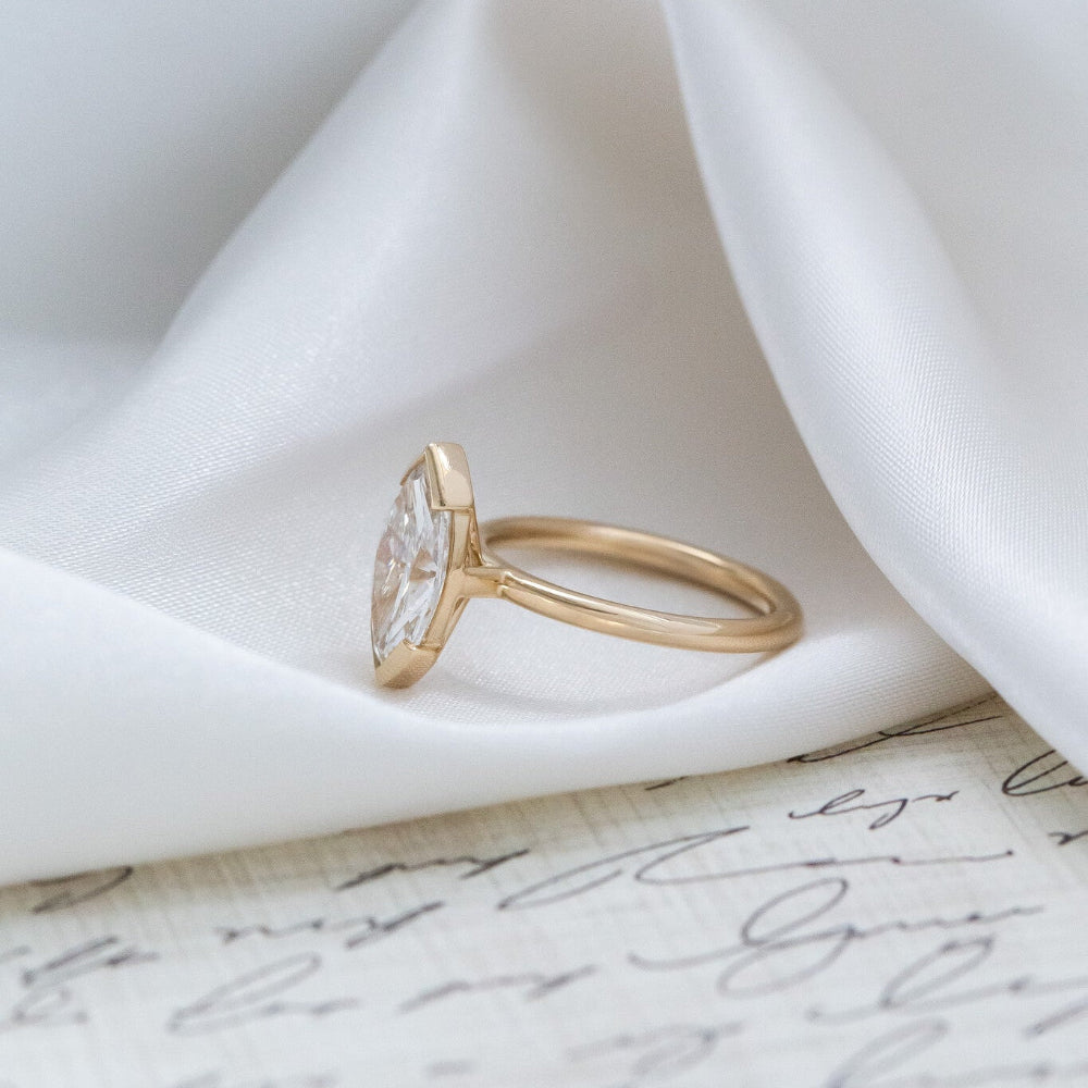 Side profile of the Zadie engagement ring with a marquise diamond on a white fabric background.