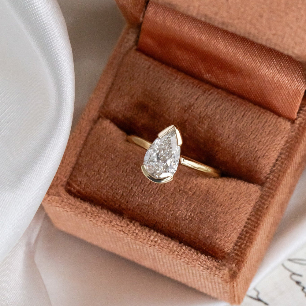 Gold Zadie engagement ring with a pear-shaped diamond in a brown jewelry box.