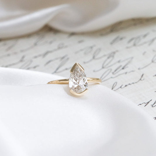Gold Zadie engagement ring with a pear-shaped diamond on a white fabric background.