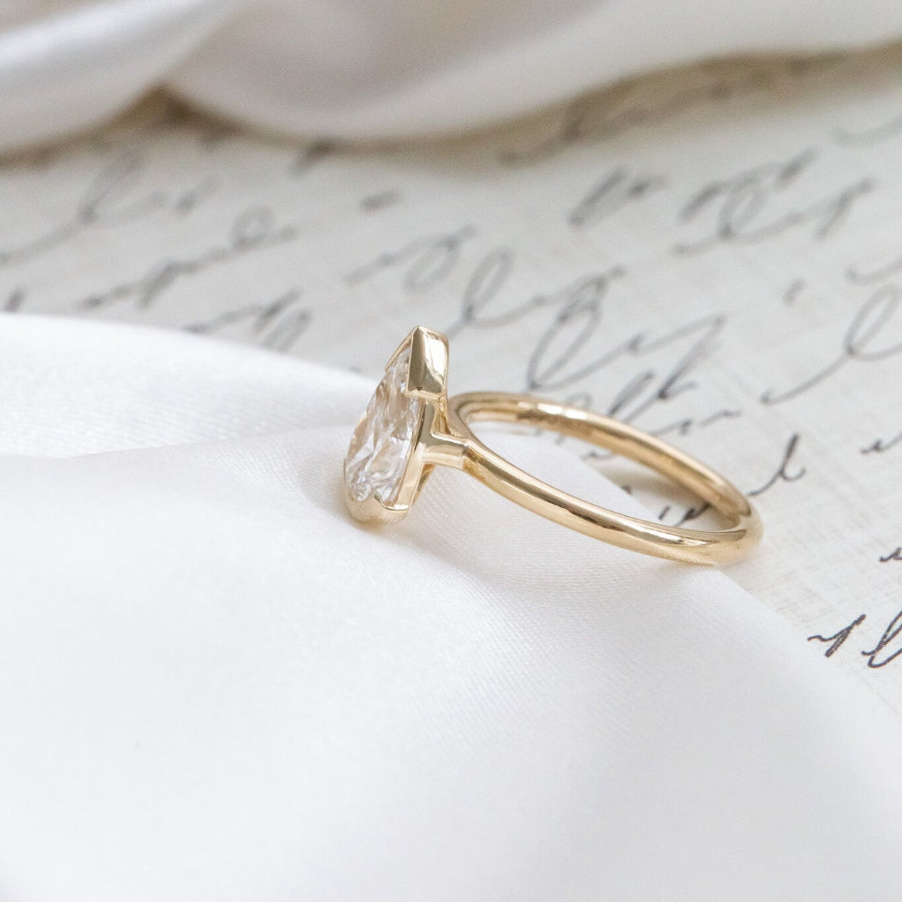 Gold Zadie ring with a pear-shaped diamond on a white fabric background.