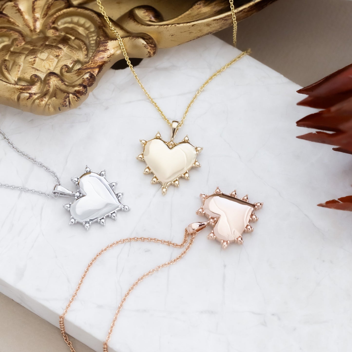 Heart-shaped necklaces in white gold, yellow gold, and rose gold on a marble surface.
